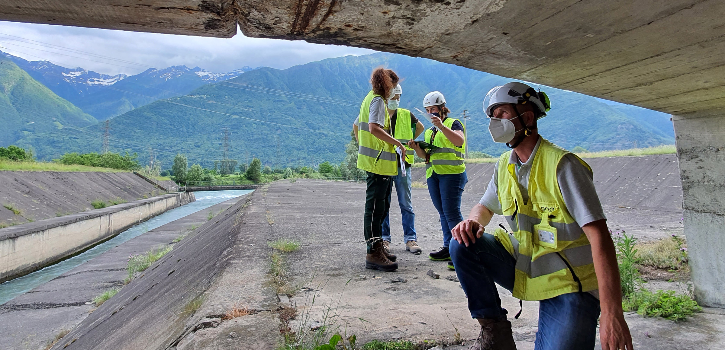 un grupo de trabajadores con chalecos de alta visibilidad y cascos realiza una inspección en una infraestructura ubicada en las montañas